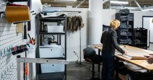 A person working at a large table inside a warehouse unit at Elevator’s North Kansas City facility, with shelving, packing materials, and production tools visible.
