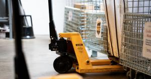 Close-up of a yellow pallet jack next to metal shipping carts in Elevator’s North Kansas City logistics area.