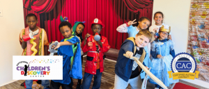 A group of children in colorful costumes is posing together in front of a theatrical backdrop, showcasing creativity and playfulness.