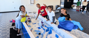 Children engage in playful activities at a water table, exploring structures and having fun in a colorful, well-lit space.