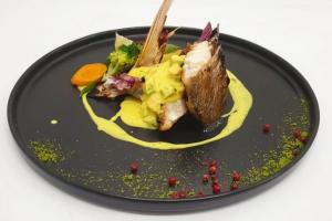 Fine-dining gourmet fish dish by Chef Kevjano Shehaj, featuring an upright seared fish fillet with creamy yellow sauce, assorted vegetables, and decorative seasoning on a black plate.