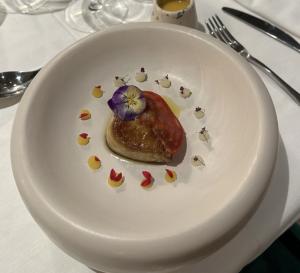 A single elegantly arranged portion with floral accents and precise drops of sauce in a white bowl, attributed by the user to Chef Kevjano Shehaj.