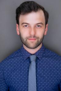 Seth Eliser in a blue shirt and tie is looking directly at the camera with a neutral expression