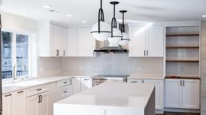 Modern kitchen featuring a sleek island with waterfall countertop, white cabinetry, stainless steel appliances, and pendant lighting in a bright, contemporary space.