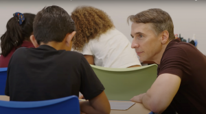 Richard and a student are both sitting at a table while the student works on a math problem.