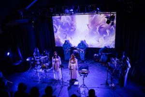 La banda de rock progresivo de nueve miembros Fantompass se presenta en vivo en el escenario, con trajes de inspiración medieval y un fondo animado proyectado durante la canción "Gates of Glory".