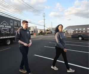 The husband and wife team behind Cool Hand Movers walking in front of two moving trucks in Red Hook, Brooklyn.
