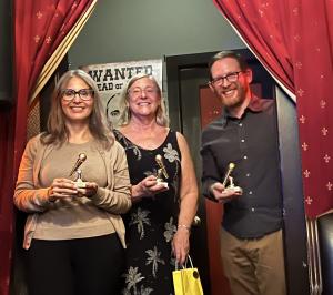 Three people holding trophies smile at the camera.