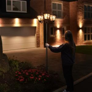 Person adjusting an outdoor lamp post in front of a modern brick house at night