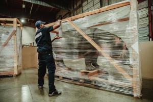 Professional mover from NOR-CAL Moving Services wrapping furniture with protective plastic in warehouse