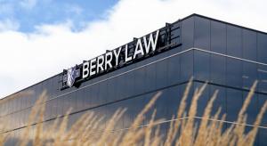 Exterior view of the Berry Law office building with the Berry Law sign mounted on a modern glass facade, seen against a blue sky with tall grasses in the foreground.