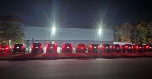 A long row of black luxury SUVs parked at night with their red taillights illuminated in front of a large warehouse building.