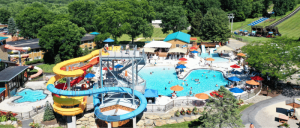Aerial view of a vibrant water park featuring a large swimming pool, twisted water slides, and colorful umbrellas, with visitors enjoying the sun.