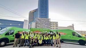 SERVPRO of Naples Marco Island restoration team in safety vests and hard hats standing with green branded vans in front of modern high-rise building