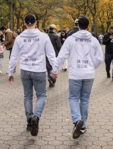 Two people walking hand in hand wearing white hoodies with “Wear Your Heart on Your Sleeve” text and heart graphics on the back.