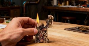 A close-up view of the Thorens Steampunk lighter in use, highlighting exposed gears, aged metal textures, and the deliberate visibility of its mechanical structure.