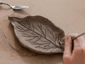 A piece of pottery clay that was made by hand with a leaf pattern carved into it during the molding and shaping process.