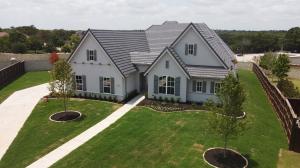High-angle view of a gray home at 2300 Palmetto Way featuring dark gray tile roofing and matching dark gutters along the roofline, overlooking a manicured green lawn with a concrete walkway and young trees.