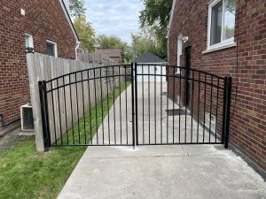 Black metal driveway gate installed between two residential buildings, providing controlled access to a driveway.