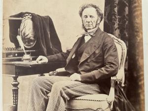 A man from the 1840s sitting at a desk, looking at the camera