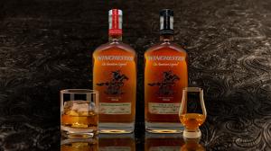 Two bottles of Winchester Bourbon—Kentucky Straight and Double Oaked—displayed on a dark textured surface with a rocks glass and a Glencairn glass filled with bourbon.