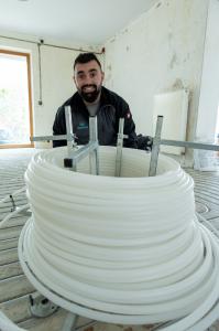 Ein Mitarbeiter von Nordwærme Fußbodenheizungen mit einem Rohr bereitet die Verlegung in einem Bestandsgebäude in Braunschweig/Niedersachsen vor.