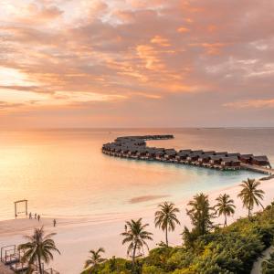 Aerial view of the sunset in the Maldives, with ocean views and overwater villas in the distance.