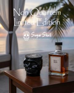A candle in a black sugar skull jar and a bottle of bay rum sit on a side table in a cabana on a tropical beach