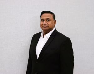 Clayburn Figredo, founder of Cleaning Edge Solutions, standing in a dark suit against a light background.