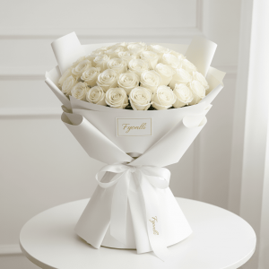 Fyonlli Expands Online Flower Delivery and Gifting Services across the United Arab Emirates 14 A bouquet of elegant white roses wrapped in smooth white paper, tied with a ribbon, sits on a round table against a soft white background, exuding elegance.