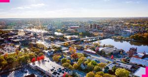 Aerial view of downtown Rockford, Illinois, with the Rock River running through the city, multiple bridges, mid-rise buildings, and dense autumn trees.