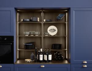 A close-up of an open shelving unit with a dark wood interior, surrounded by matte navy blue cabinet doors with gold cup handles. The shelves are neatly organized with black bowls, patterned cups, and wine bottles.