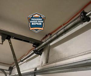 A close-up of a technician wearing a red Milwaukee work glove performing maintenance on a Genie Intellicode garage door opener unit, featuring the Pasadena Garage Door Repair logo.