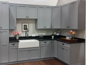 Grey shaker-style kitchen cabinets with black hardware, a white farmhouse sink, and black countertops, installed by Las Vegas Wholesalers Kitchen and Bathroom Cabinet Center.