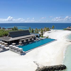 Oceanfront infinity pool beside a white-sand beach with palm trees and the Indian Ocean beyond.