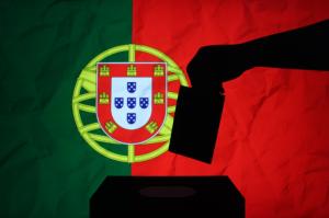 Hand placing vote into ballot box with Portugal flag in the background