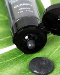 Macro close-up of Zion Health Charcoal Face Mask dispensing a dark gray activated charcoal formula onto a green leaf, showcasing the creamy, mineral-based texture.