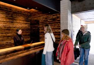 An image of a family checking into a hotel and being greeted by the receptionist. Modern design with artistic charred Cedar wood making the check-in desk and surrounding walls