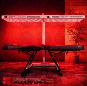 A full body red light system over a black massage table in a glowing room.