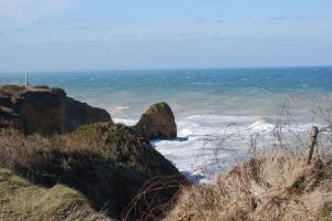 A view of waves crashing along the cliffs at Pointe du Hoc with the Ranger Monument visible in the background.