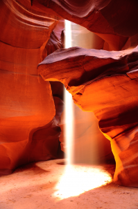 Sunlight beam shining through Antelope Canyon, highlighting layered red sandstone formations and the canyon floor below.