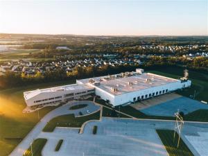 Aerial photograph of the BioTechnique pharmaceutical manufacturing facility, showing a large white industrial building with clean landscaped grounds, paved parking areas, and surrounding open acreage. The facility sits on expansive property with room for