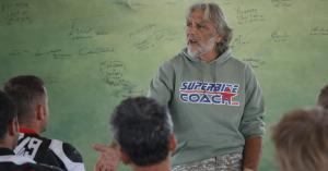 Superbike-Coach Corp instructor teaching motorcycle riders during a cornering school classroom session, with students in full riding gear.