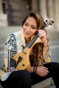 Brown haired woman holding a violin strikes a pensive pose seated steps before a cathedral