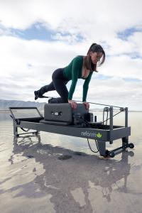 Female Model on Modern Reform MRX™ Pilates Essentials Reformer (Color: Midnight) with Mountains in the background, set in a salt lake bed.