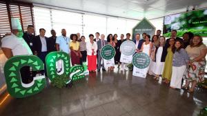 A group of representatives from SESC, SENAC, and GI International standing together in a bright hall, holding circular green and white Carbon Neutral certification signs. Large green decorative letters spelling 