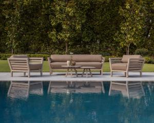 This image shows the Romeo Sofa, Romeo Club Chairs and Romeo Coffee Tables which are part of the Weathered Collection by a deep blue pool set against a backdrop of lush greenery.