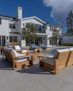 The image shows the Kuba Collection set in the backyard of a large country style white wood home. The Kuba Sofa, Kuba Club Chairs, Kuba Coffee Table and Kuba Sun Loungers are desplayed on both corners of the pool to provide a comfortable and relaxed seati