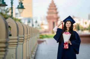 Cambodian university graduate holding bouquet and wearing cap and gown in Phnom Penh after completing degree through Love Without Boundaries Cambodia scholarship program.