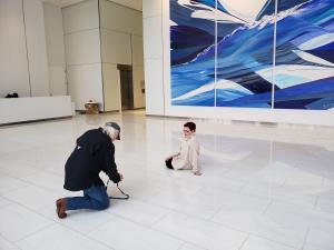 A woman sitting on the floor in front of a major, large scale painting in many blue tones, resembling waves.